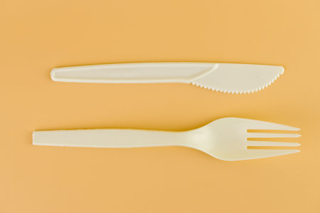 top shot close-up on soft yellow background pair of plastic white knives and forks disposable...