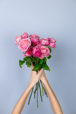 on light gray background a young blonde girl in a light T-shirt covers her face with peony roses yellow flowers for separationの写真素材