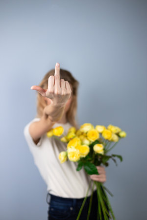on a light gray background young blonde girl refuses yellow peony roses March 8th emotions of discontent flowers for separation stop hand gesture to cameraの写真素材