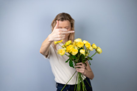 on a light gray background young blonde girl refuses yellow peony roses March 8th emotions of discontent flowers for separation stop hand gesture to cameraの写真素材