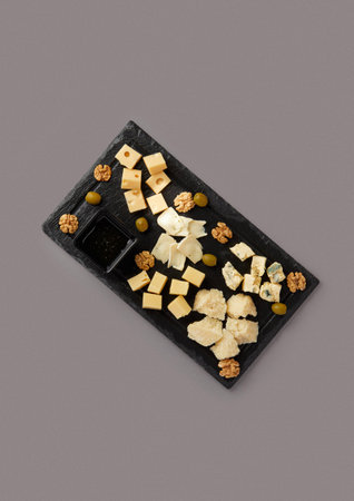 top shot on gray background black stone board with diced cheese assorted cheese plate served with honey nuts delicacyの写真素材