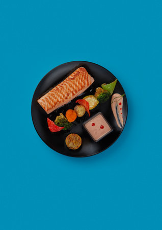 on blue background on a black plate laid out red grilled salmon fillet served with grilled vegetables and additional fish sauce professional cuisineの写真素材