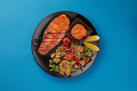 on blue background on a black plate laid out red grilled salmon fillet served with grilled...