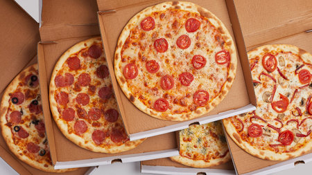 close-up cardboard boxes stand one top of the other opens with whole pizzas with different flavors pepperoni jalapeno Dorblu cheese four cheeses pizza for a large companyの写真素材