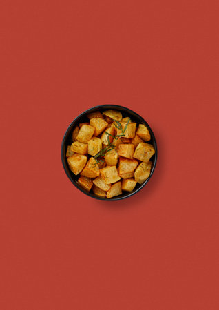 top shot on red background in a black plate, fried potatoes in round slices, rustic style, sprinkled with rosemary, aromatic side dishの写真素材