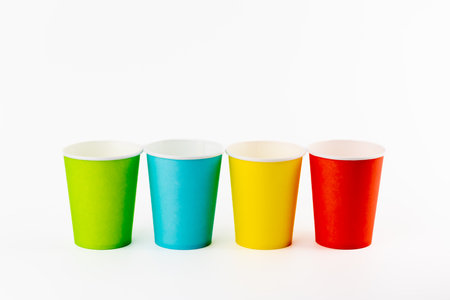 on white background, four paper cups for coffee and tea painted in red, green, yellow and blue, disposable tableware, attributes for trips, recreation and picnics, eco cups, waterproofの写真素材