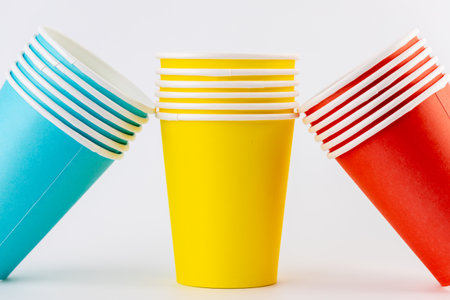 white background a stack of paper cups painted in red and blue rest on yellow disposable tableware for trips vacations and picnics eco cups waterproofの写真素材