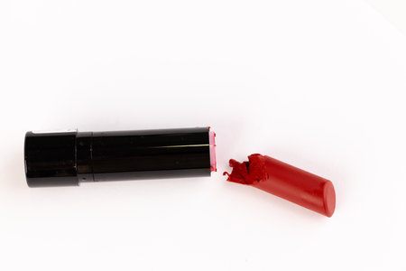 A Broken Red Lipstick in Black Tube Captured on a Clean White Background - A Close Up View of Beauty Product Disarray and Lip Color.の写真素材