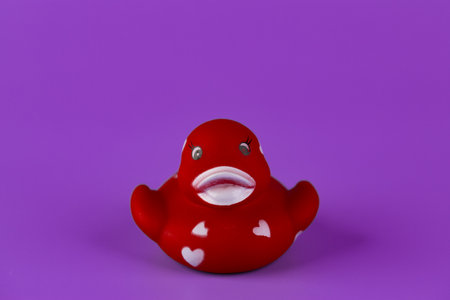 Adorable Red Rubber Duck with Hearts on a Vibrant Purple Background - A Cute Icon of Fun and Playfulness in Bath Time or Decorationの写真素材