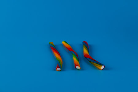 Colorful Twisted Candy Sticks on a Bright Blue Background, Perfect for Sweets Lovers and Candy Enthusiasts to Enjoy in Various Flavors and Shapes for Festive Occasions or Everyday Treatsの写真素材