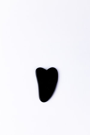 Elegant Black Heart-Shaped Tool on White Background for Skincare or Massage Purposes, Ideal for Relaxation, Gua Sha Technique, Enhancing Beauty Rituals and Self-Care Sessionsの写真素材