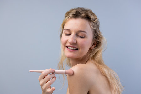 Captivating Beauty: A Young Woman Applying Makeup Gracefully with a Brush, Radiating Confidence Against a Soft Gray Background, Highlighting a Natural Beauty Aestheticの写真素材