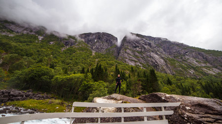 Majestic Mountain Landscape: A Solo Adventurer Amidst Lush Greenery and Dramatic Peaks under Cloudy Skies in a Serene Natural Setting, Perfect for Exploration and Reflectionの写真素材