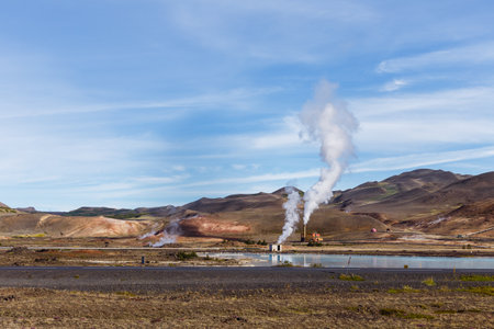 Breathtaking Scenery of Volcanic Landscape with Steam Emanating from Geothermal Plant Surrounded by Majestic Mountains and Clear Blue Skies in a Peaceful Natural Settingの写真素材