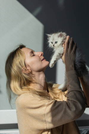 A Tender Moment of Connection Between a Woman and a Playful Kitten in Soft Natural Light, Capturing Joy and Affection in a Cozy Indoor Setting with Gentle Shadowsの写真素材