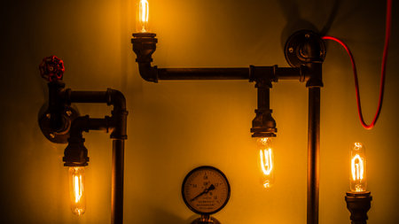 Industrial-Style Home Decor Featuring Vintage Edison Bulbs, Metal Pipes, and a Decorative Gauge on a Warmly Lit Wall for a Trendy Atmosphereの写真素材