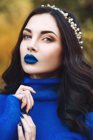 Sensual portrait of a beautiful woman with a blue sweater with accessories on head in a park.の写真素材