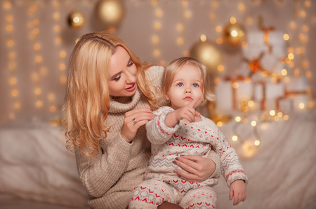 Merry Christmas and Happy holidays! Small kid with mom sitting in decorated room with gifts and lights and enjoying. Daughter and mother spending holiday together. Family New Year conceptsの写真素材