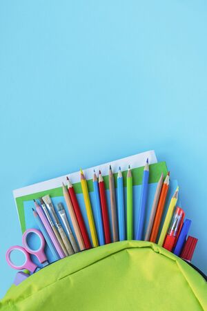 Green backpack with school supplies on blue background. Back to school concept. Top view, copy space.の写真素材