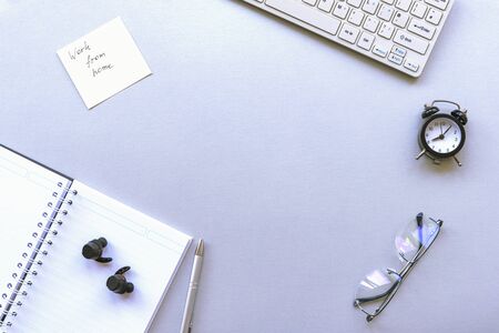 Cozy workplace with keyboard, notepad, wireless headphones, alarm clock and glasses on grey background. Work from home concept. Top view, Flat lay, copy space.の写真素材