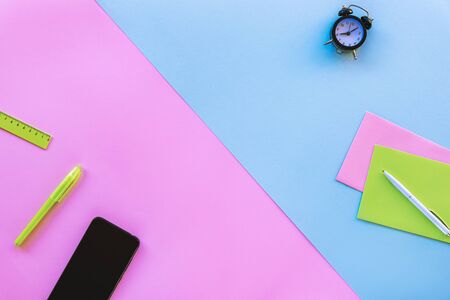 Mobile phone, pen and office accessories on pink and blue background. Work from home concept. Top view, flat lay.の写真素材