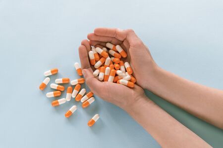 Child or womans hands holds white and orange colored pills against blue background, top view