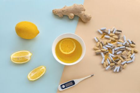 Lemon, ginger, pills, thermometer and cup of tea on yellow and blue background. Alternative remedies and traditional pills, natural medicine vs conventional medicine concept. Top view, flat layの写真素材