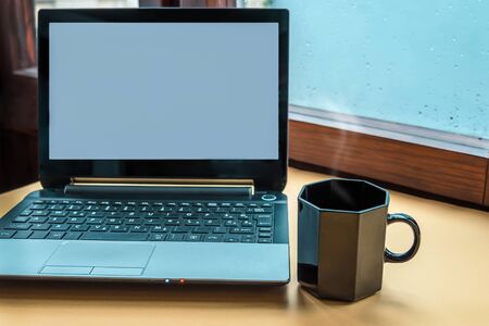 Computer and a cup of hot beverage against the window with raindrops background. Cosy workplace, freelance. Copy space.の写真素材