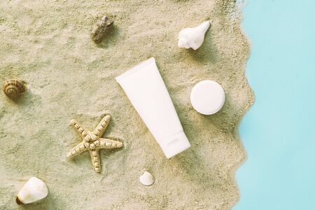 White containers of cosmetic cream and serum on the sand. Starfish and shells, blue backgroundの写真素材