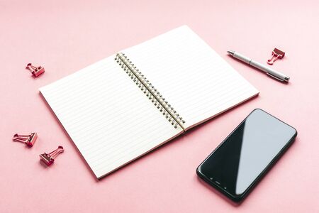 Blank spiral notepad on a pink background with mobile phone, pen and paper clips. Workplace, business or education concept.の写真素材