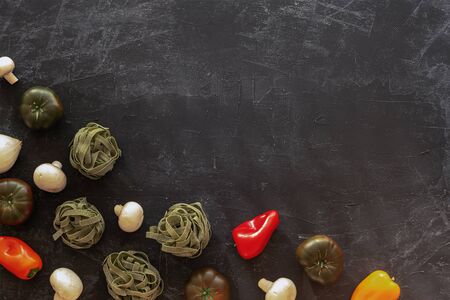 Raw green spinach spaghetti, vegetables and mushrooms on a black table. Italian cuisine concept, healthy food. Top view, flat layの写真素材