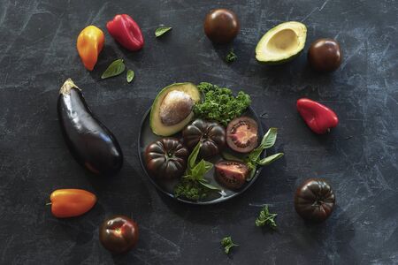 Tomatoes, avocado, eggplant and other vegetables and herbs on chalkboard backdrop, healthy vegan food. Black background.の写真素材