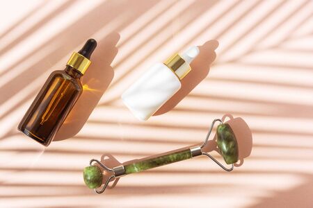 Flat lay of beauty products: facial roller, cosmetic oil and serum on coral background in palm leaves shadow, top view. Natural cosmetics and beauty treatment.の写真素材