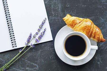 Cup of coffee with croissant, notepad and lavender flowers on black background, top view, flat lay, copy spaceの写真素材
