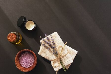 Lavender blossom, sea salt, cream jar, towels and essential oil on black background, top view, flat lay, copy space. Aromatherapy, spa and wellness concept.の写真素材
