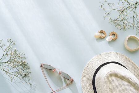 Flat lay with womens accessories on blue background. Sunglasses, straw hat, earrings, bracelet and gypsophila flowers. Top view, copy space.の写真素材