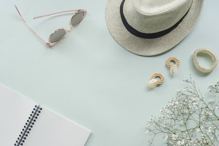 Flat lay with womens accessories on blue background. Sunglasses, straw hat, earrings, bracelet,...