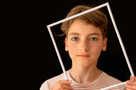 Beautiful teenage girl with short hair holding white picture frame on black background.の写真素材