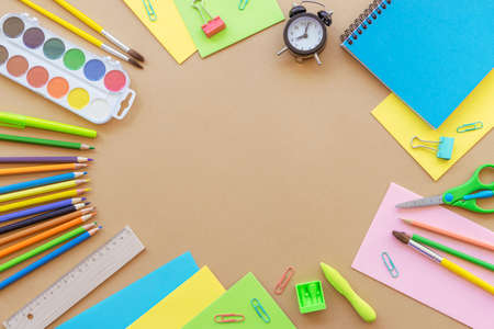 School supplies stationery, colour pencils, paints, alarm clock, paper on beige background. Back to school concept. Top view, flat lay.の写真素材