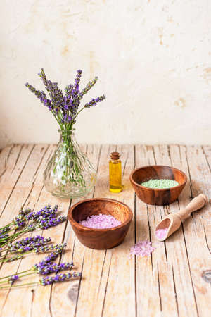 Bottle of essential oil and bowls with sea salt on wooden table. Lavender cosmetics, spa and wellness concept. Selective focus.の写真素材