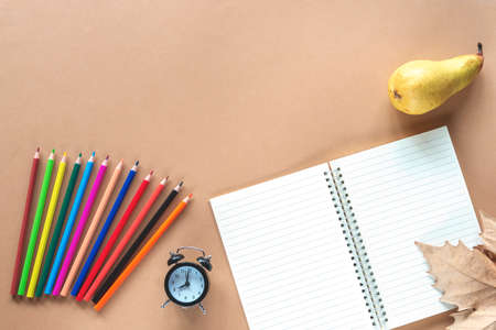 School supplies, alarm clock, pear and autumn leaf on light brown background. Back to school concept. Top view, flat lay, copy spaceの写真素材