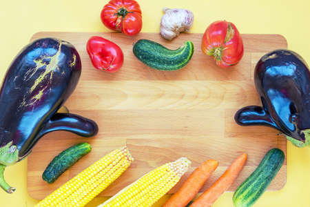 Home grown vegetables, ugly food on wooden cutboard, yellow background, copy space.の写真素材