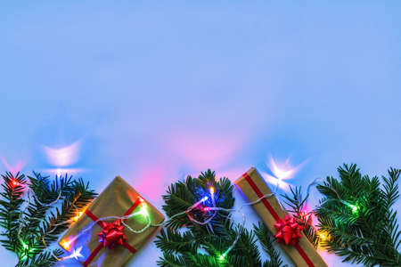 Boxes with gift and Christmas fir twigs, garland with colorful lights, neon color background. Top...
