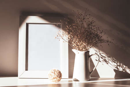 Blank picture frame and Gypsophila flowers in light with shadows, mock up. Still life