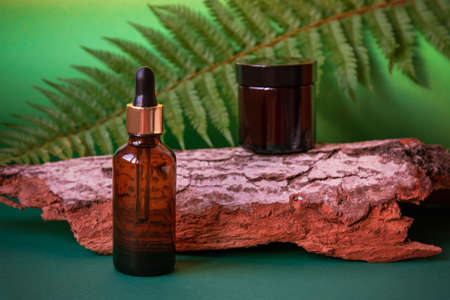 Cosmetic facial cream jar and serum bottle on the background of natural wood and fern leaves. Natural organic skin care products. Front viewの写真素材