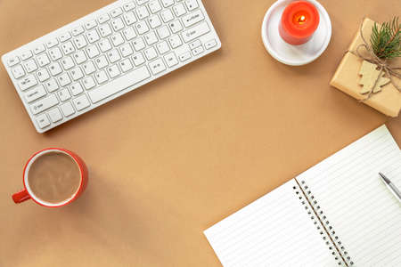 Cozy workplace with keyboard, notepad, gift in a box, candle, cup of coffee or cocoa on beige background. New year or Christmas holidays concept. Top view, flat lay, copy space.の写真素材
