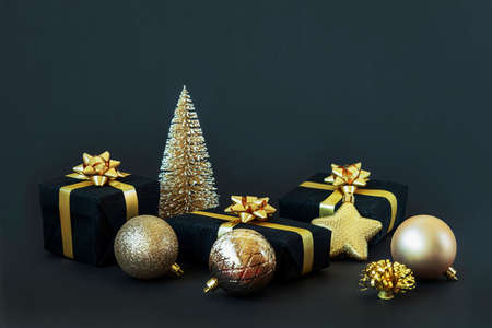Black gift boxes with golden ribbon, balls and toy Christmas tree on black background. New Year concept. Close up, copy space.の写真素材