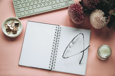 Woman workplace with chrysanthemum flowers, blank notepad, computer keyboard, eyeglasses and candle. Top view, flat lay. Pink background.の写真素材