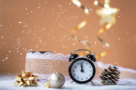 Alarm clock, Christmas tree toys and pine cone on beige background with snow. Christmas decorations, New Year concept. Shallow depth of field.の写真素材