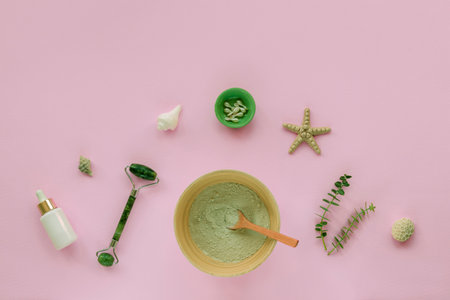 Natural organic cosmetics: bowl with clay, serum or cosmetic oil bottle, face roller, beauty capsules and eucalyptus leaves on pink background. Home spa concept. Top view, flat lay, copy space.の写真素材